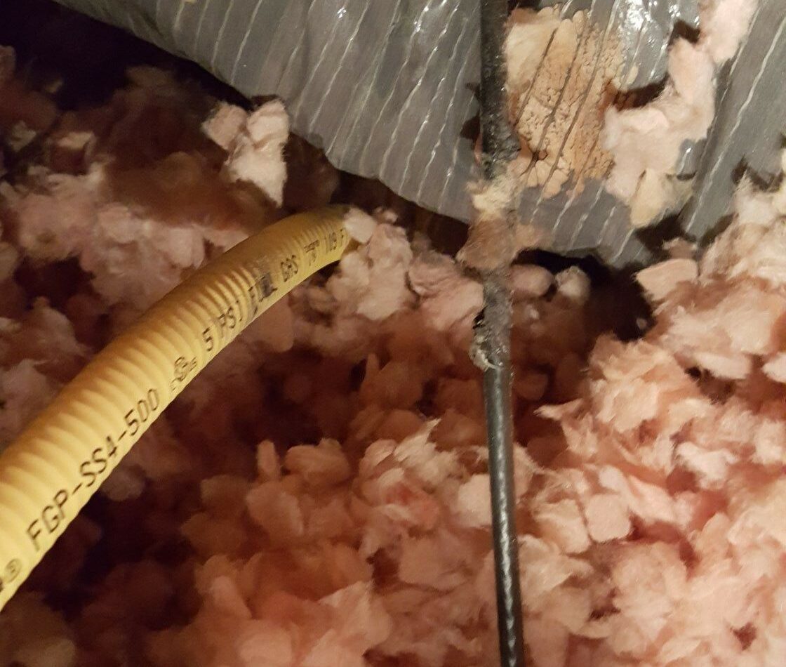 Roof gas leak caused by nearby power cable. Pink fiberglass insulation surrounds a a yellow gas supply line, located only a few inches from a black power cable.